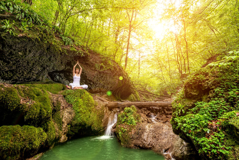 女人在瀑布边练习瑜伽。Sukhasana姿势