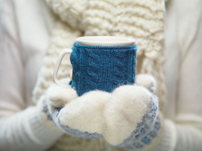 一位女士手戴白色和蓝色手套，手里拿着一个舒适的编织杯，里面有热可可、茶或咖啡。冬季和圣诞节时间概念。