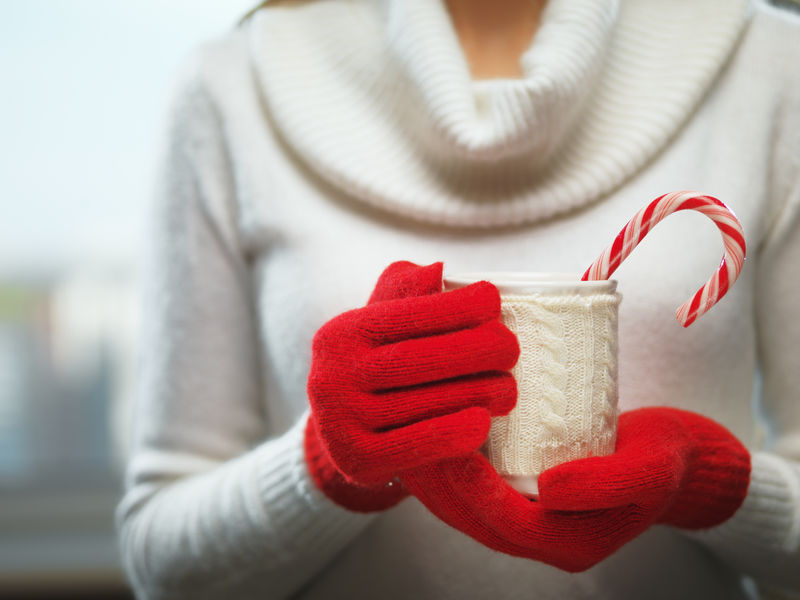 女人手上戴着毛红色手套，手里拿着一个舒适的杯子，里面有热可可、茶或咖啡和一根甘蔗糖。冬季和圣诞节的概念。