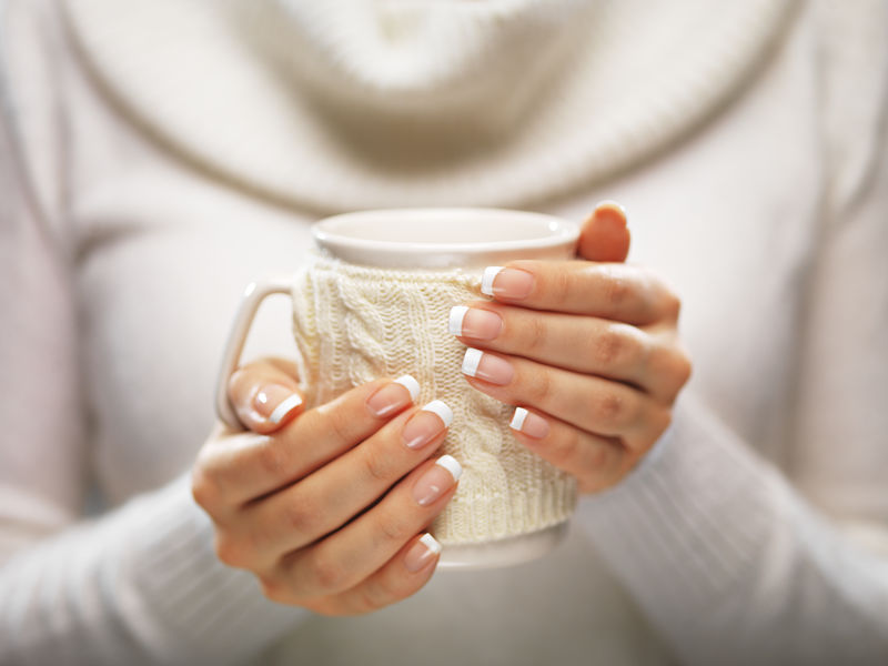 女人手拿着一个舒适的针织马克杯，优雅的法式指甲设计。冬季和圣诞节时间概念。