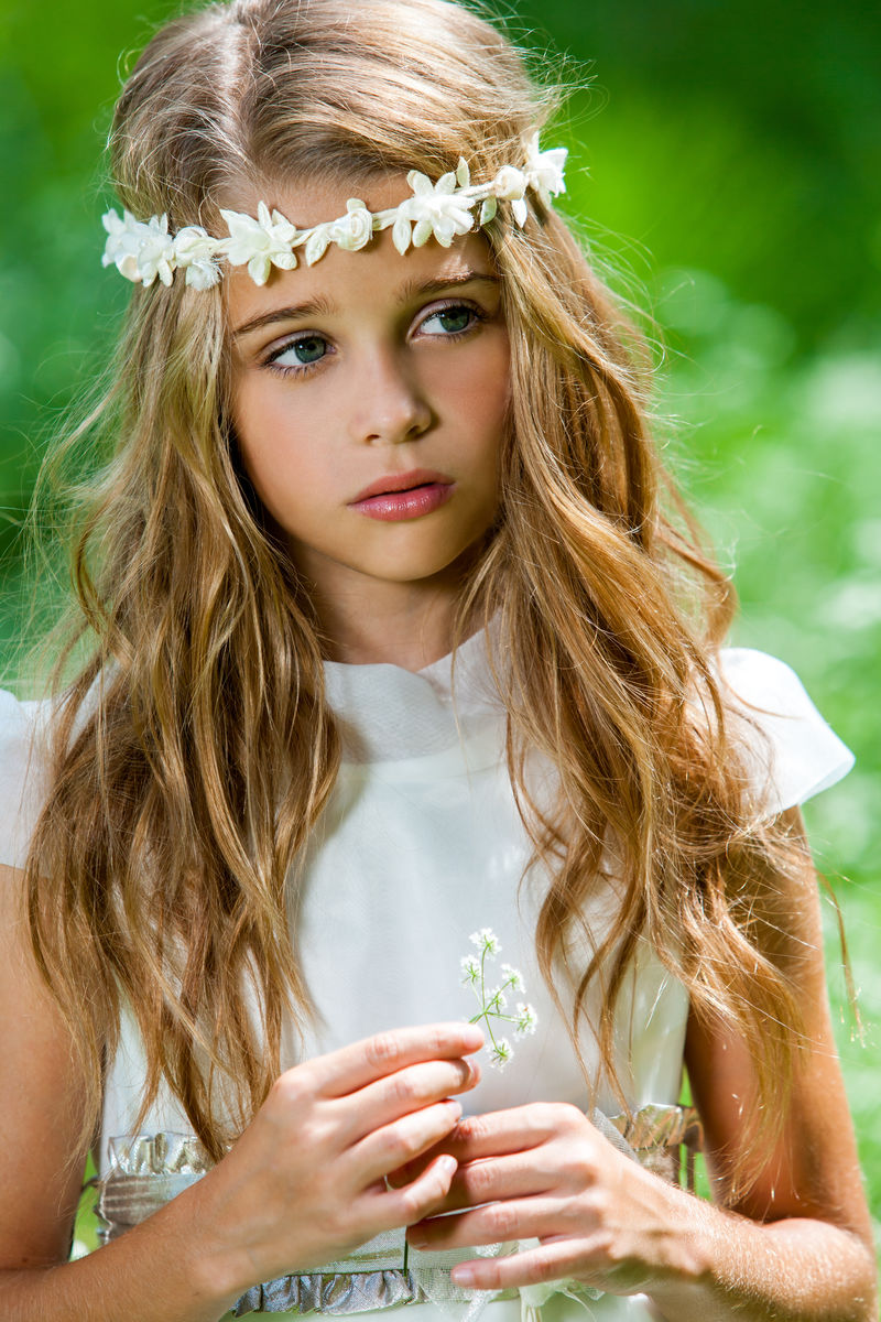 一个穿着白色连衣裙拿着花的可爱女孩。