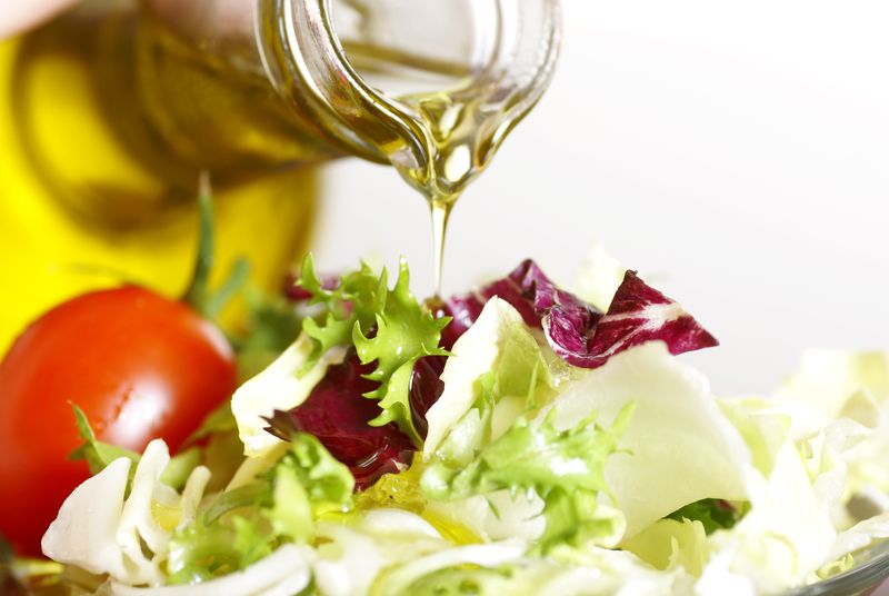 用倒入橄榄油和蔬菜沙拉的瓶子的特写镜头