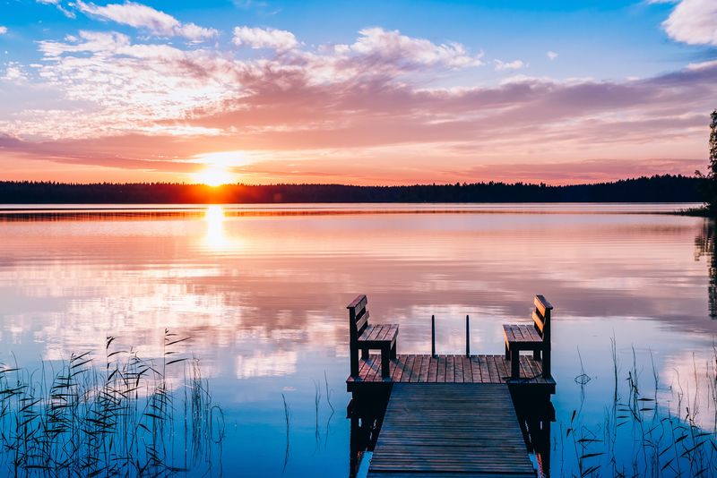湖面上有木制长凳的长码头的田园风光。日落或日出。