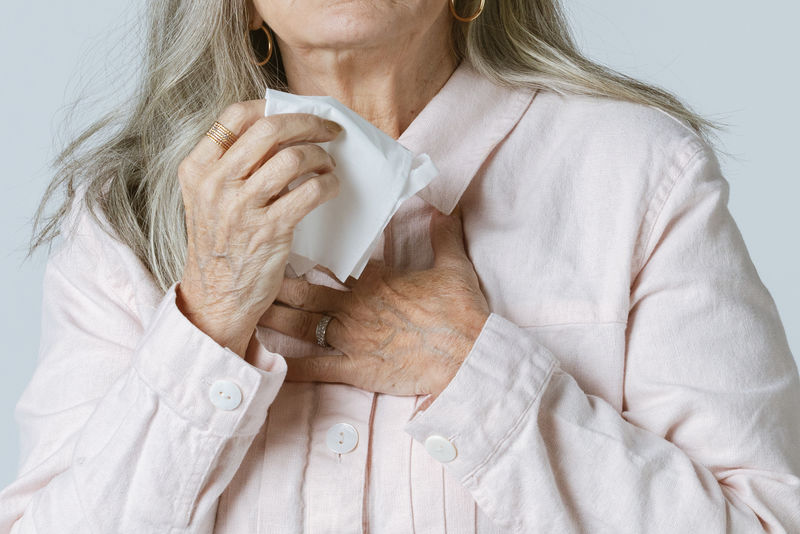 感染冠状病毒的老年妇女用纸巾擤鼻子