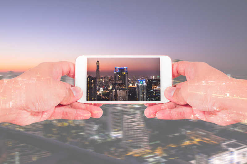 双手使用智能手机和城市夜景的双重曝光