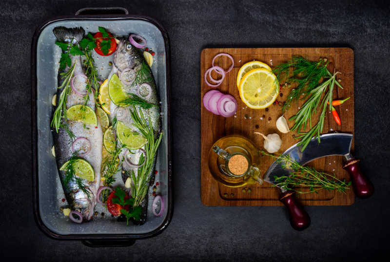 案板上的烹饪配料和锅中配料腌制的两条新鲜的鱼