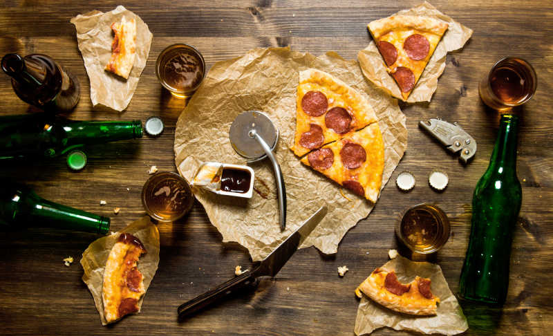 在一张木桌上的意大利腊肠比萨饼和啤酒四人俯视图