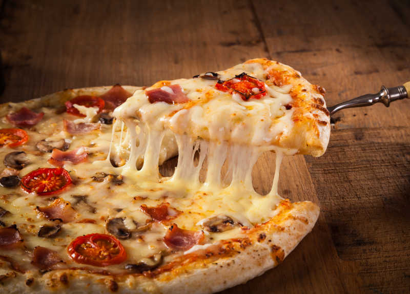 热腾腾的融化的奶酪的比萨片在一块粗陋的木桌上