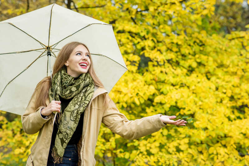 女人带着伞在秋天的公园微笑