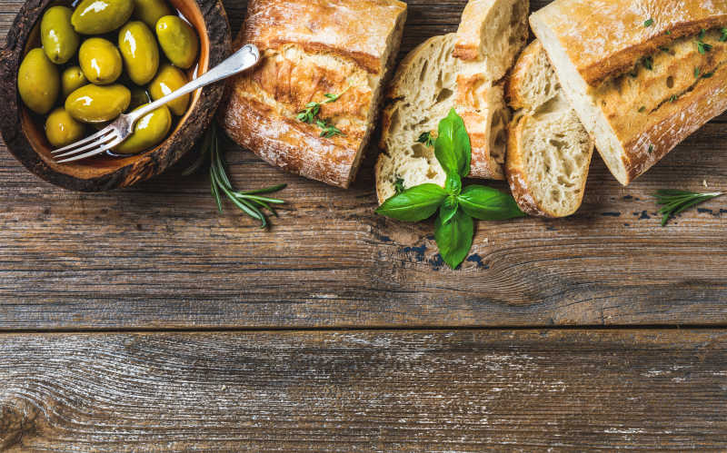 木桌上的切开的面包和绿色橄榄
