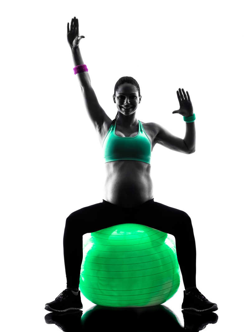白色背景下坐在瑜伽球上健身的孕妇