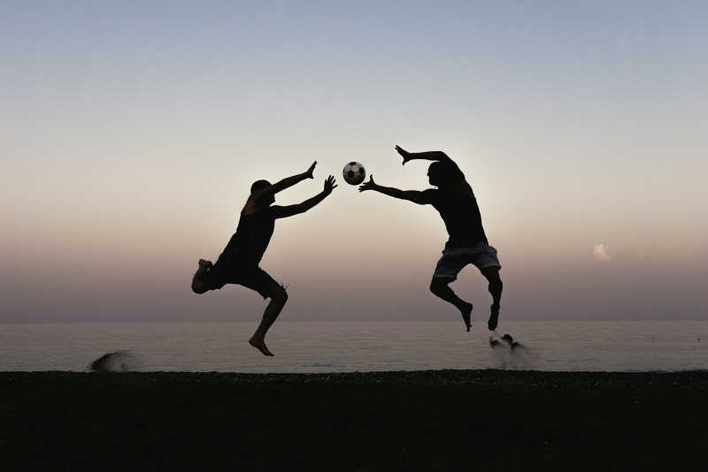 沙滩上正在踢足球的两个男人剪影
