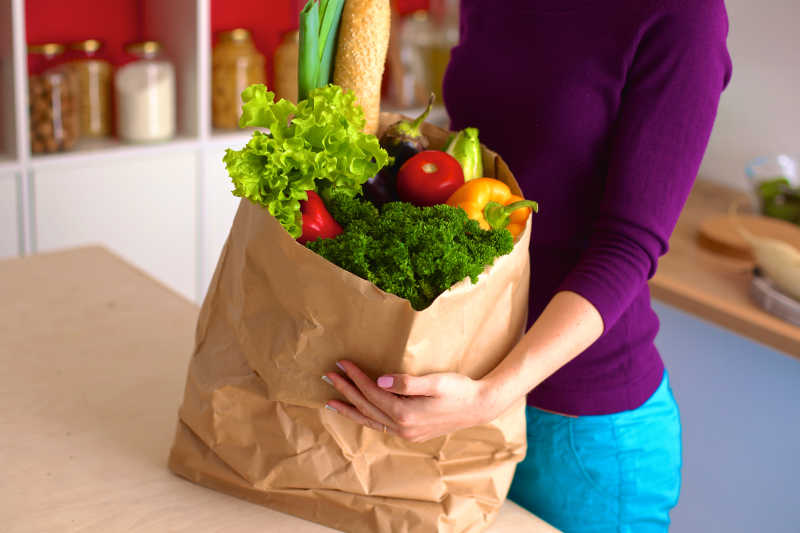 女人手里拿着一个满是水果和蔬菜的纸质购物袋