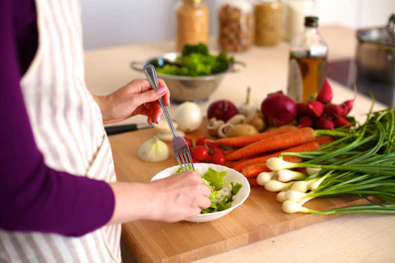 年轻女人在厨房木板上做蔬菜沙拉