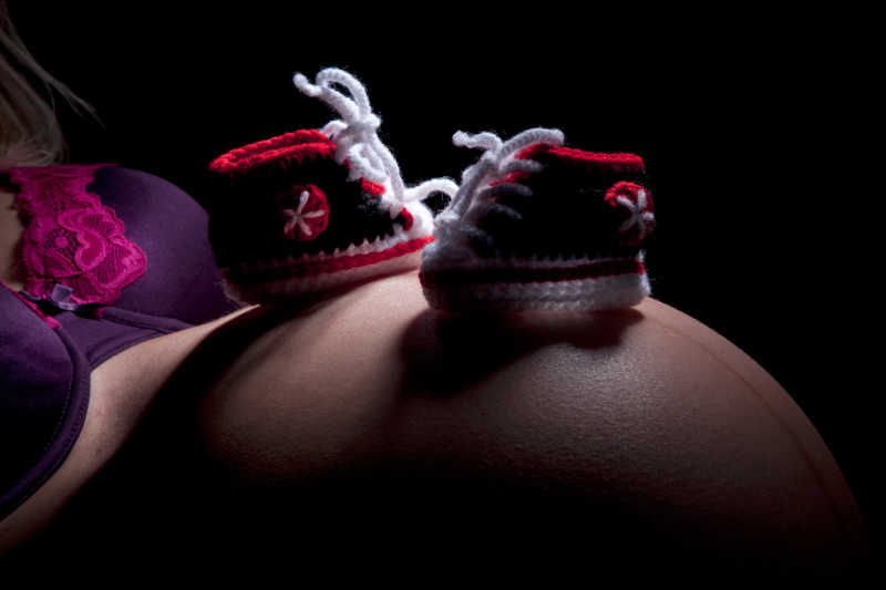 黑色背景下躺着的孕妇腹部的婴儿鞋
