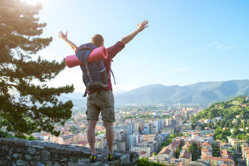 年轻的旅行者张开双臂站在俯瞰城市风景的高地上
