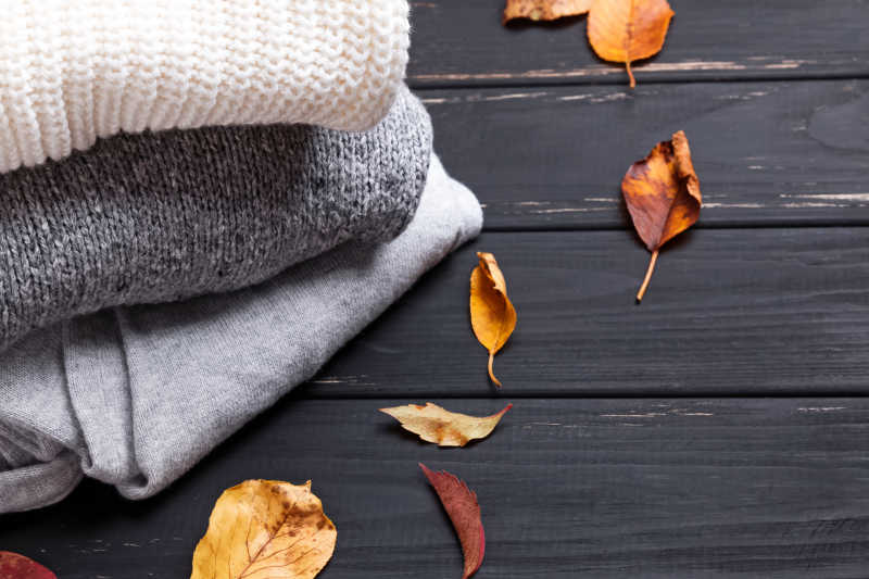 黑色木制背景下的舒适毛衣和秋叶