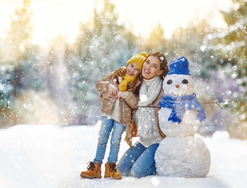 母亲和孩子在雪地堆雪人