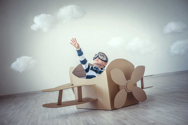 坐在飞机纸模型里幻想飞行的男孩