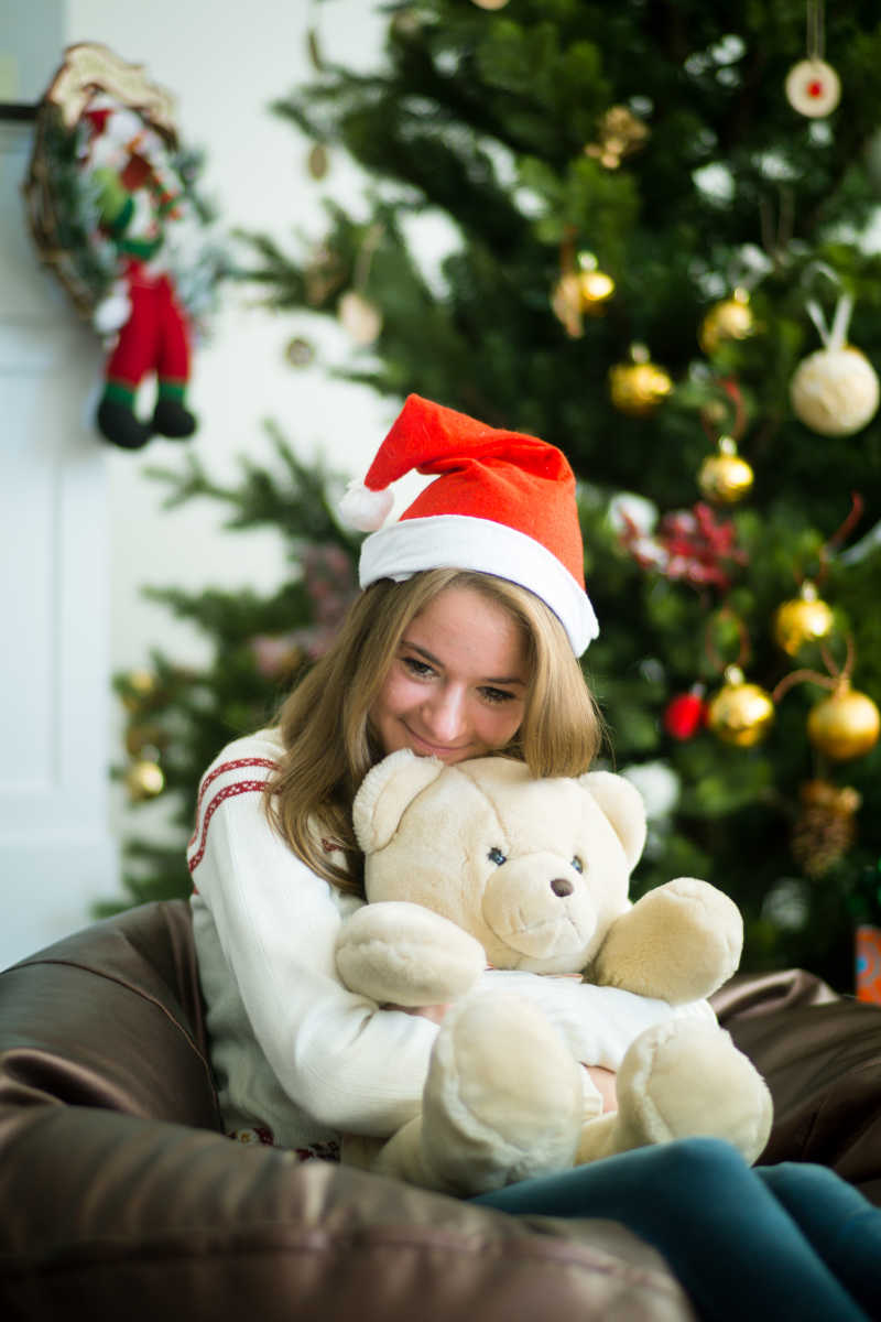 沙发上抱着泰迪熊微笑的圣诞女孩