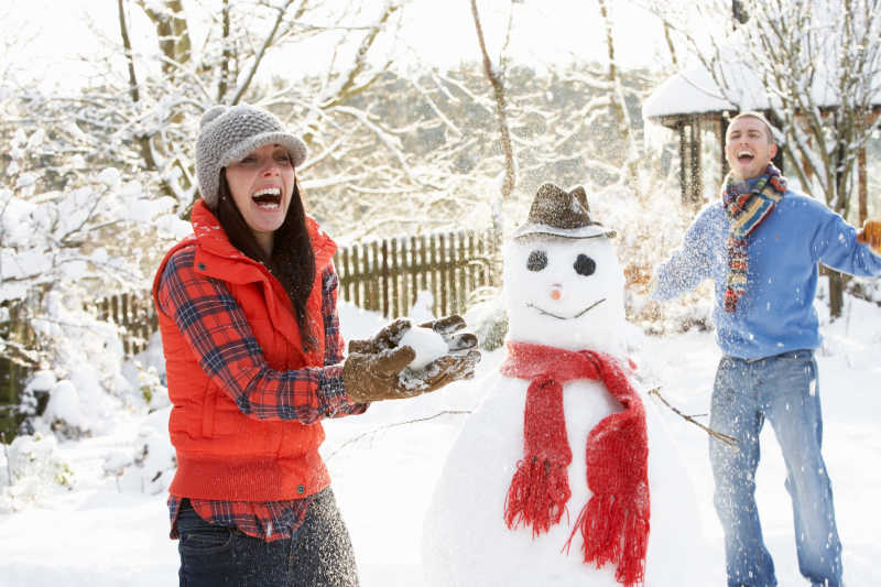 在花园里打雪仗堆雪人的年轻夫妇