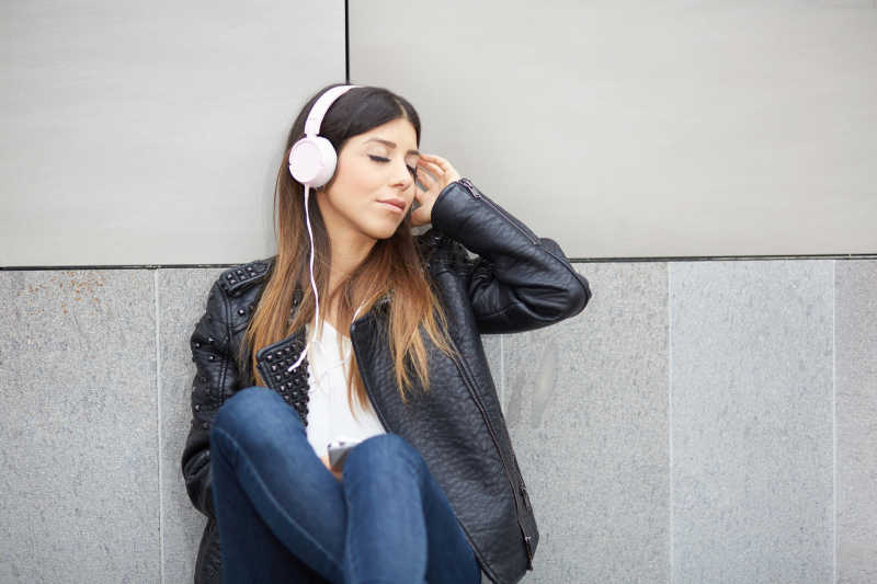 靠着墙戴耳机享受音乐的女人