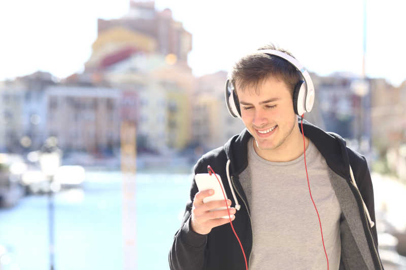 在户外戴耳机听音乐的年轻男人