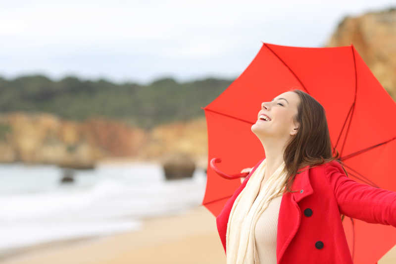 在海滩撑着红色雨伞的美女