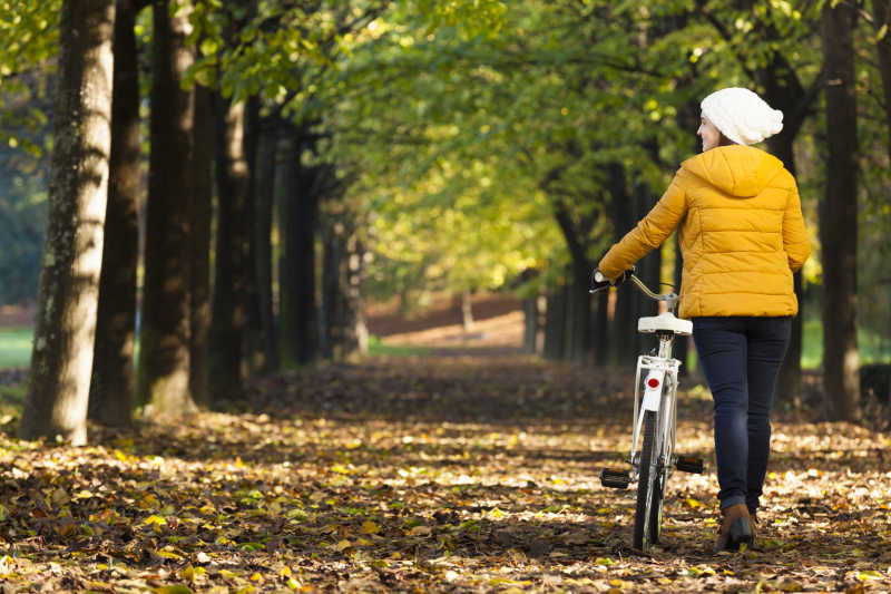 秋季的树林里扶着自行车散步的美女