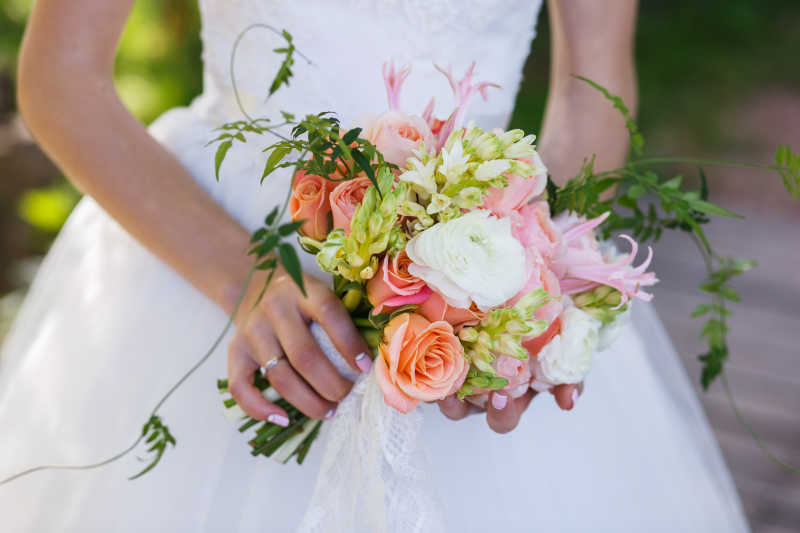 户外背景下穿着白色婚纱的新娘手中的美丽婚礼花束