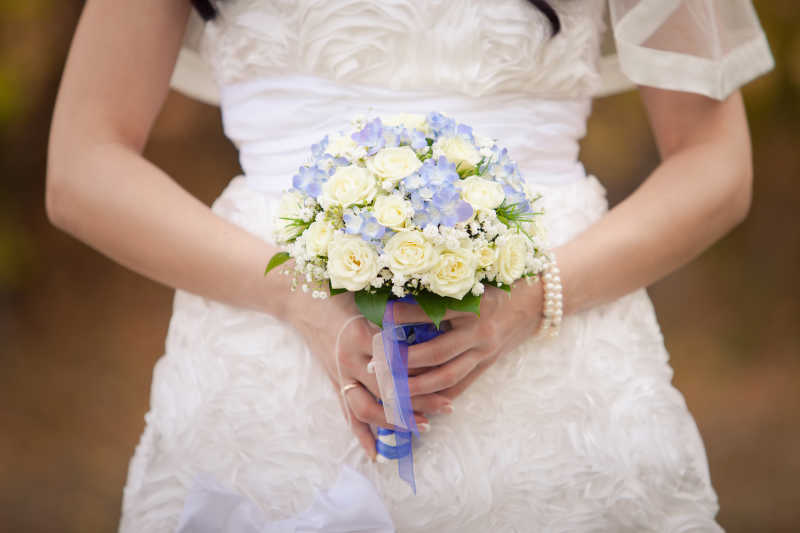 钱换粉色背景下穿着白色婚纱的新娘手中的美丽婚礼花束