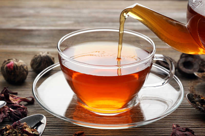 木制背景下的玻璃茶壶往茶杯里倒茶
