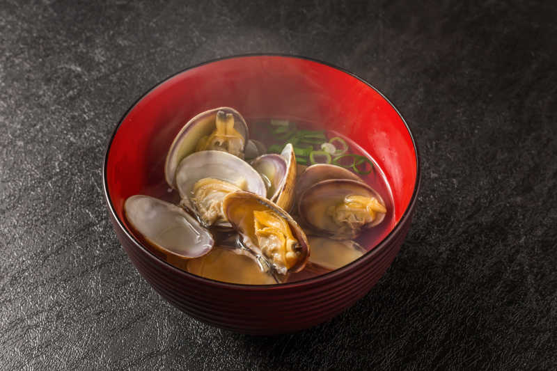 黑色桌上红色碗里的蛤蜊海鲜汤