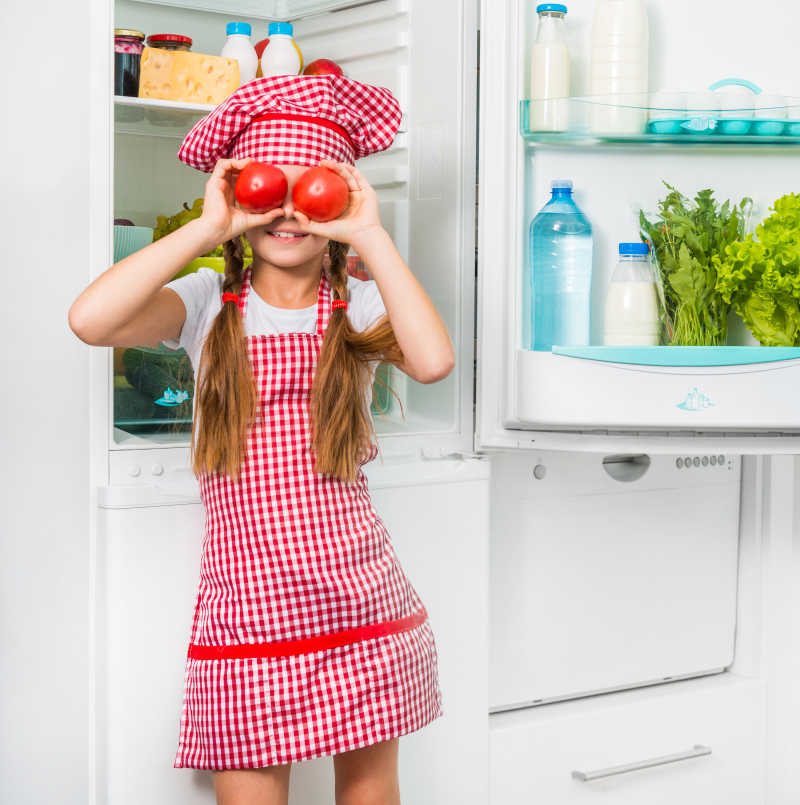 冰箱旁边的厨师小女孩拿着西红柿