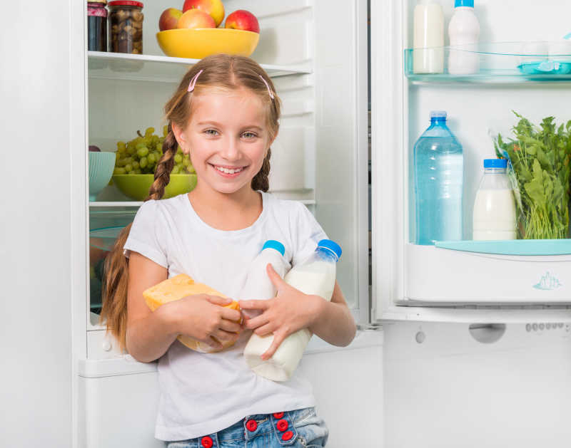冰箱旁边的小女孩拿着奶酪和牛奶