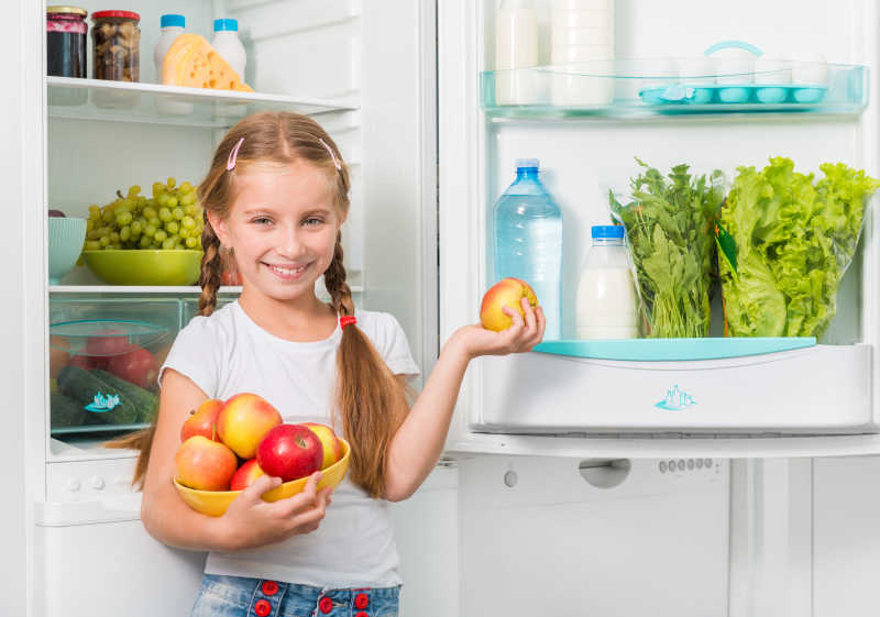 冰箱旁边拿着苹果的小女孩
