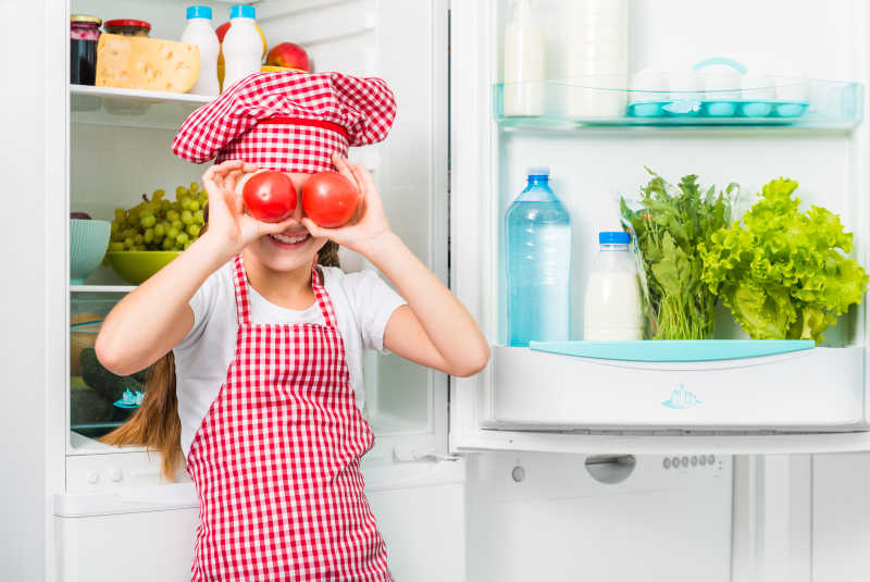 小女孩从冰箱里拿出两个西红柿