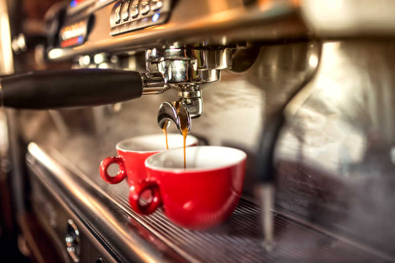 两个红色杯子在咖啡机下接咖啡