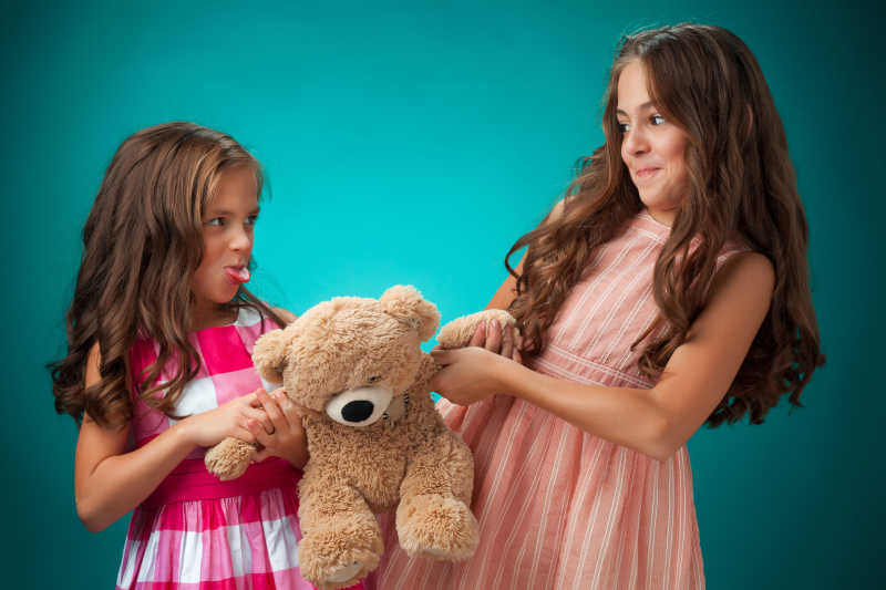 蓝色背景下抢小熊玩具的两个可爱的小女孩