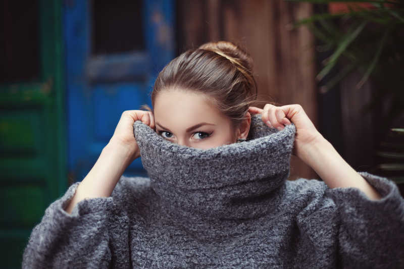 穿着针织高领毛衣的年轻女子遮住脸