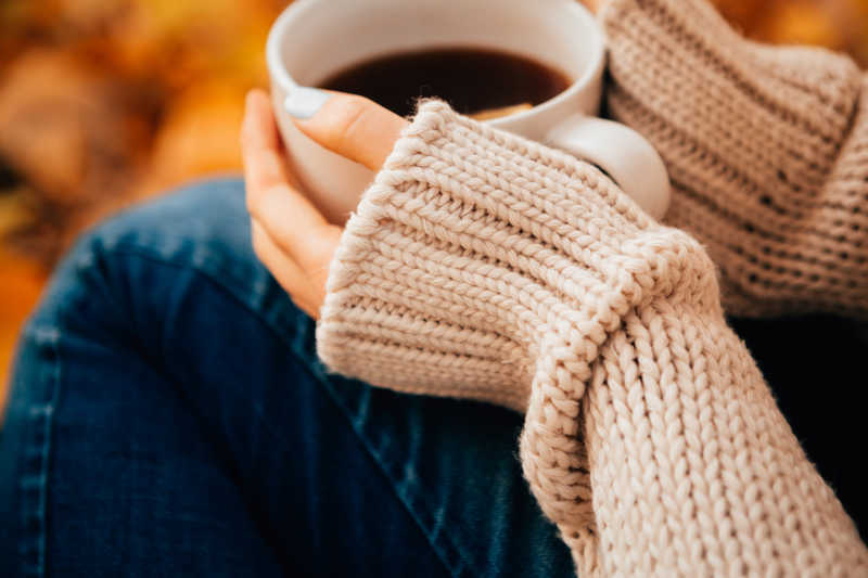 穿毛衣和牛仔裤的年轻女子手里暖着一杯茶