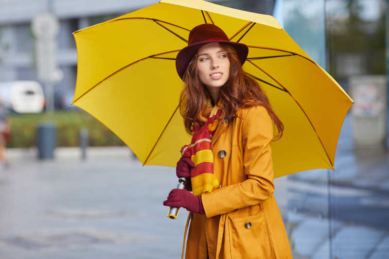 秋天美丽的年轻女子在街头打着雨伞
