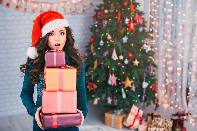 圣诞树背景前拿着礼盒惊讶的美女