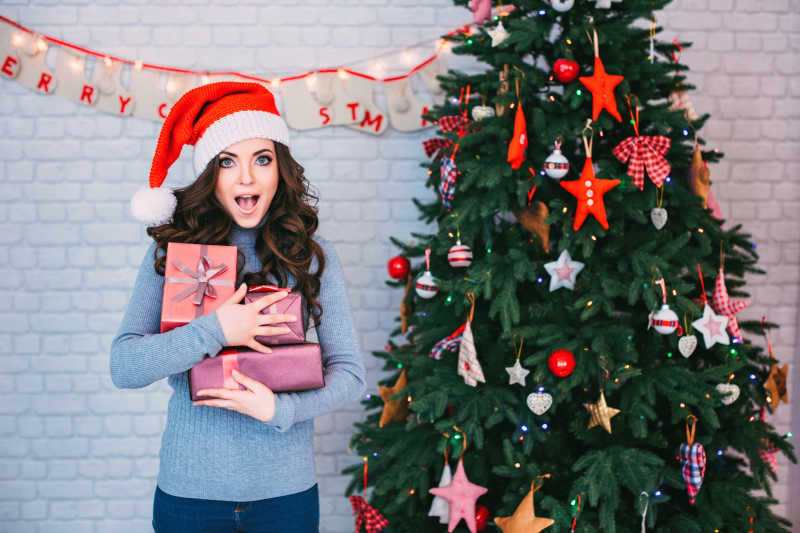 在圣诞树旁抱着礼盒的年轻美女