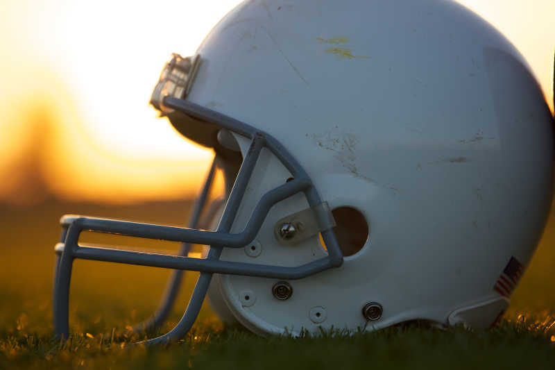 日落时放在草地上的美式橄榄球头盔
