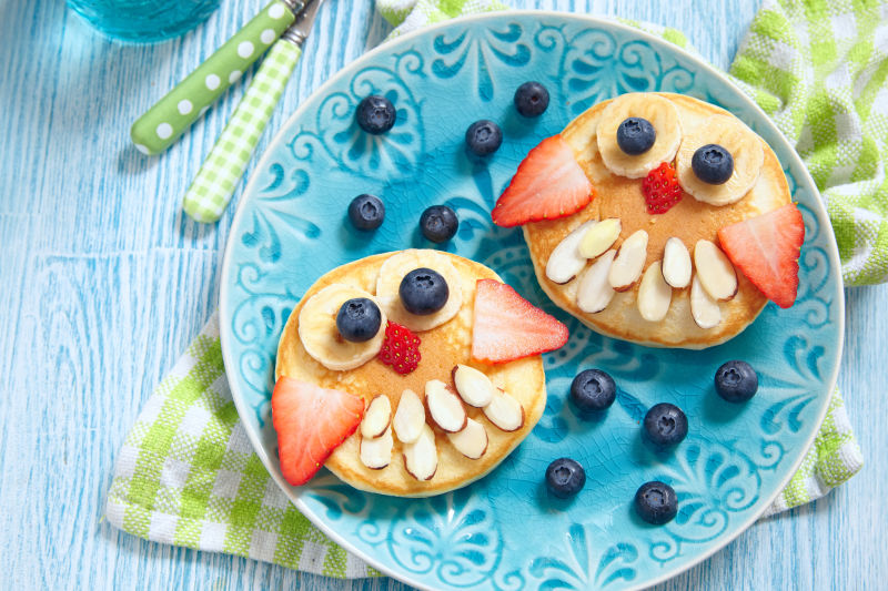 蓝色盘子里用热松饼和水果摆成的猫头鹰图案