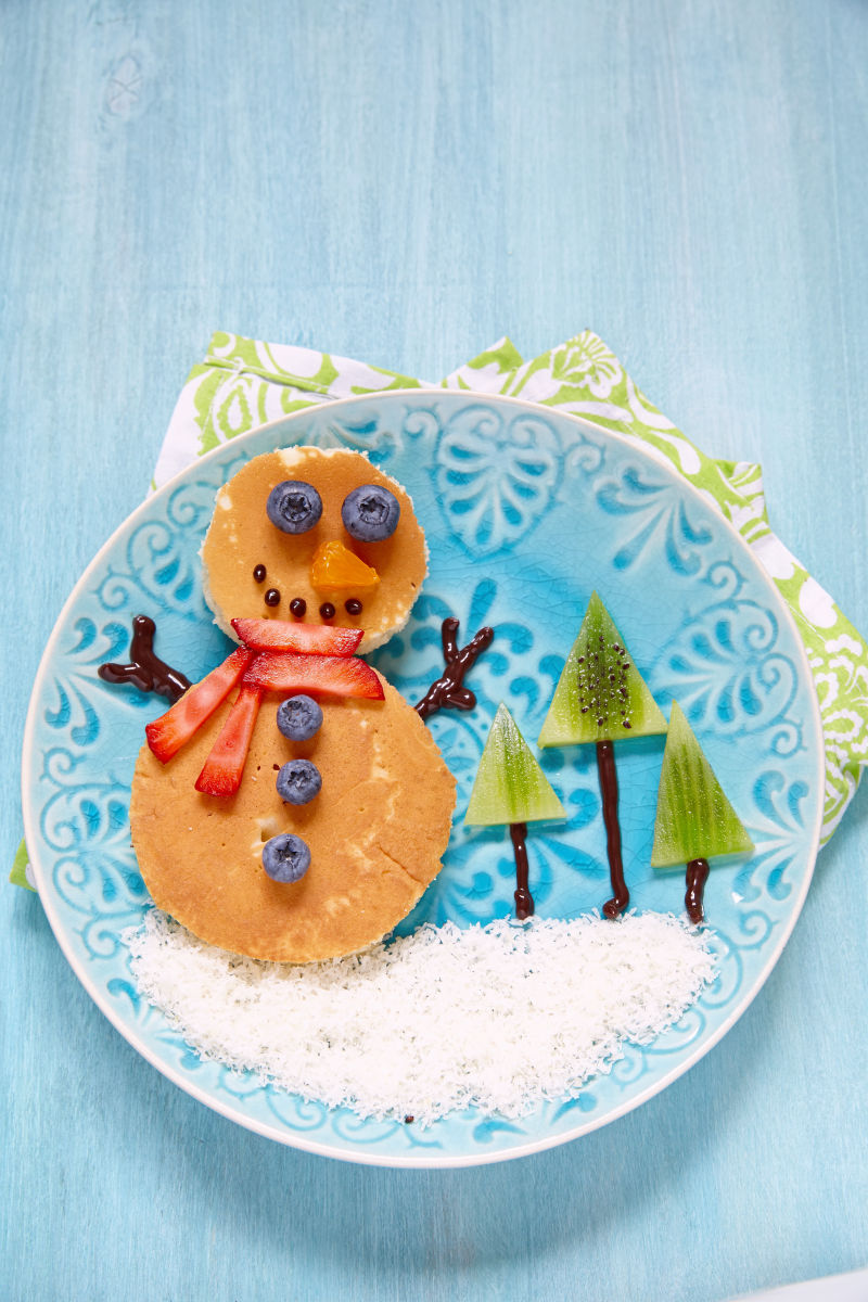 蓝色盘子里用热松饼和水果摆成的雪人和圣诞树