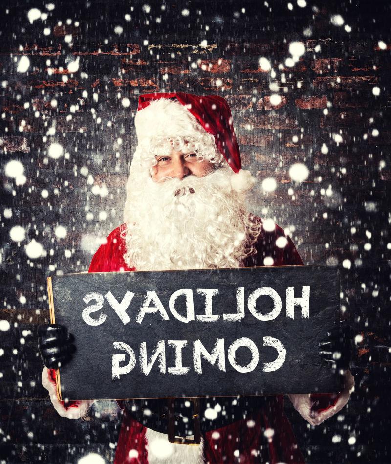 木色有雪花降落的背景下圣诞老人拿着写着放假的小黑板