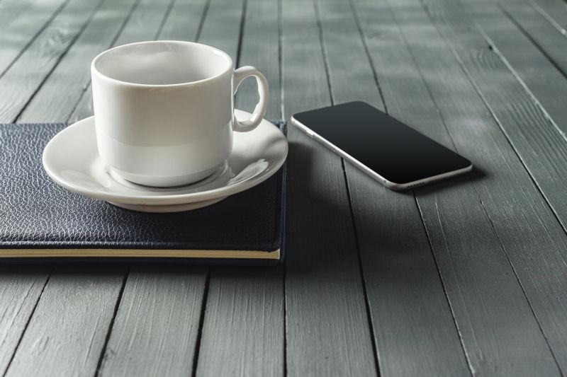 棕色木桌上的咖啡杯和笔记本还有手机