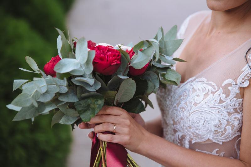 戴着结婚戒指和白礼服的新娘手中拿着美丽的婚礼花束